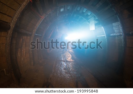 dusted tunnel in coal mine, silhouette of miner with flashlight