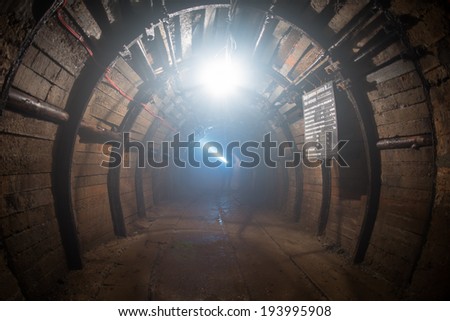 dusted tunnel in copper mine, silhouette of miner with flashlight