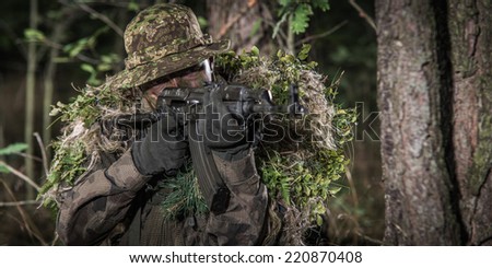 portrait of soldier wearing camouflage, in wood, aiming with automatic weapon