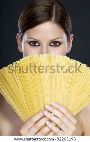 Portrait of a young beautiful woman holding a fan of spaghetti in front of her face with both hands
