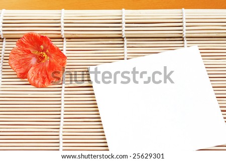 A piece of paper with a flower arranged on a bamboo mat.