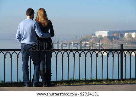 A young loving couple watching on water, sky is blue and clear