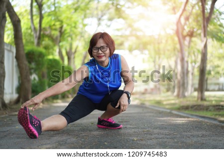 Senior asian woman stretch muscles at park and listening to music. Athletic senior exercising together outdoor. Fit senior runners stretching before running outdoors.
