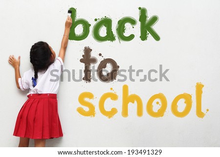 girl holding a paint brush painting back to school text on wall