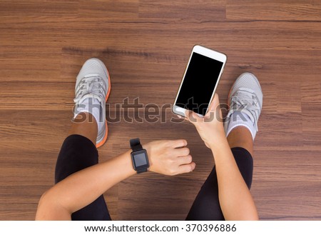 Fitness woman hand with wearing watchband touchscreen smartwatch with holding mobile phone, View from above studio shot on wooden floor background