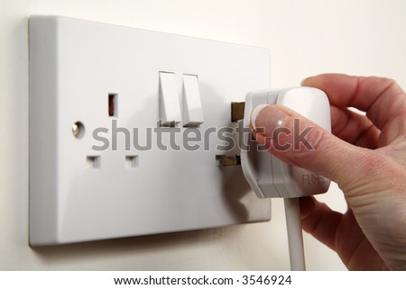 UK plug about to be plugged into a white wall socket