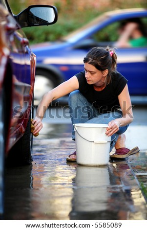 Young woman washing the wheel of a red car with a blue car in the background