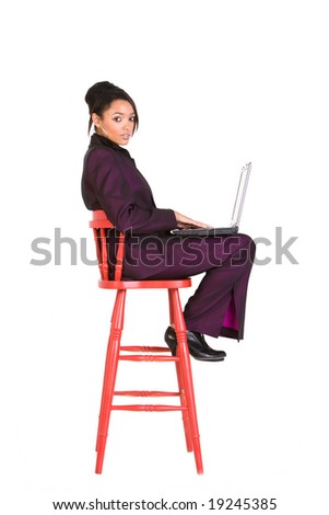 Young businesswoman sitting on red stool using a laptop computer. Model is looking at the camera