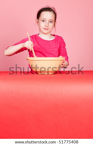 Young girl mixing a cake mixture on a pink background