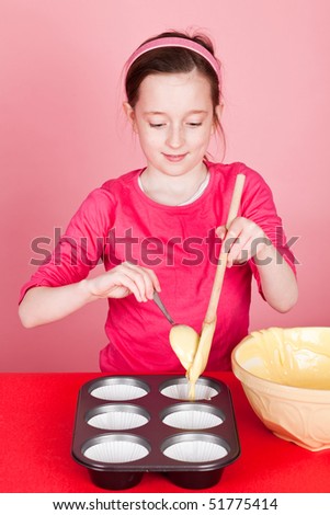 Young girl spooning the cake mixture into cake mounds