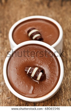 Two chocolate mousses in a white pots with a chocolate curl
