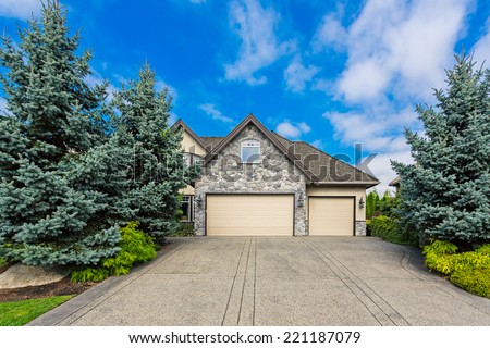 Custom built luxury house with nicely trimmed and designed front yard, lawn in a residential neighborhood in Canada. Double garage doors view.