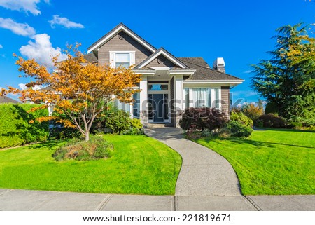 Custom built luxury house with nicely trimmed and designed front yard, lawn in a residential neighbourhood in Canada. Beautiful fall tree with yellow leaves, blue sky, sunny day.