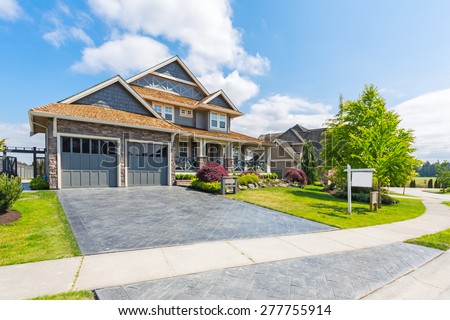 Custom built luxury house for sale with nicely trimmed and designed front yard, lawn in a residential neighborhood in Canada. For sale sign in front of the house by real estate agency.
