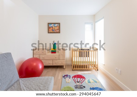 Empty nursery room with a crib, red ball, toys, carpet and couch.