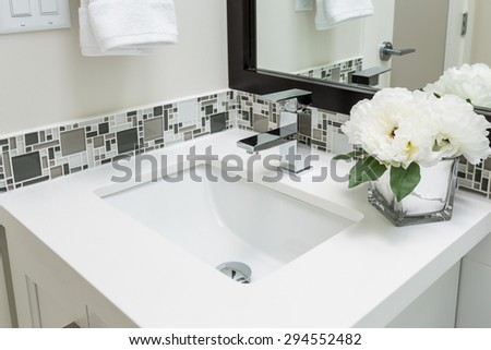 Fragment of a luxury bathroom with flowers and towels. View of a white modern sink. Interior design.
