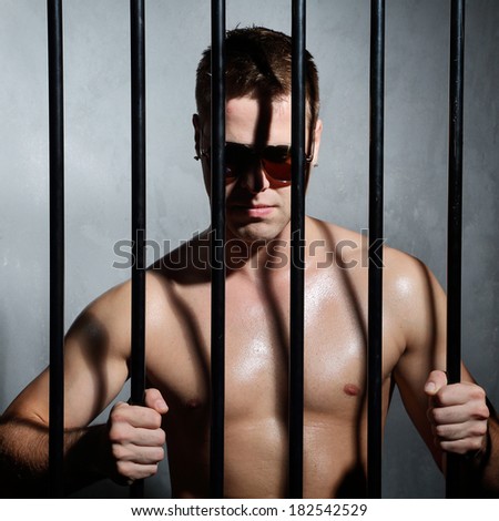 Sexy man behind iron prison bars with glasses