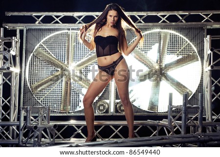 very sexy and beautiful top model in black lingerie on a stage posing with a huge turbo ventilator behind her were the smoke and stage lights are coming trough