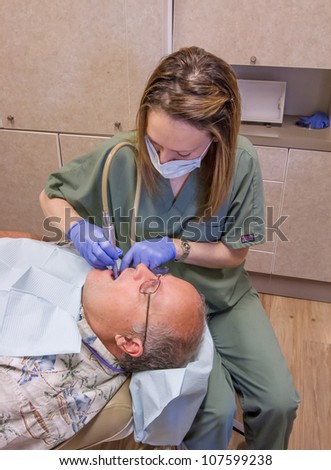 Senior man is getting his teeth checked and cleaned by the dental hygienist at his dentist\'s office.