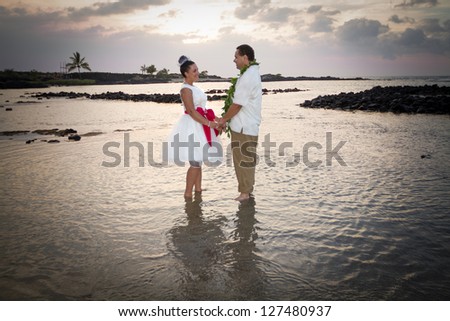 Newlywed couple standing in the warm, shallow waters of Hawaii. Horizontal portrait.