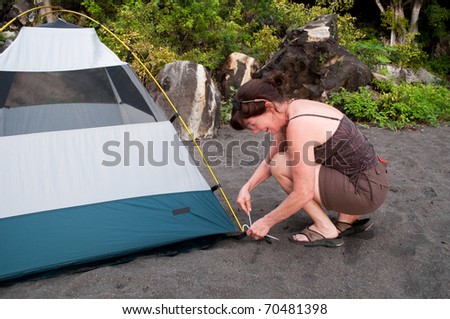Woman demonstrates how to pitch a 2 person tent on a black sand beach campsite.