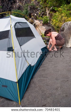 Woman demonstrates how to pitch a 2 person tent on a black sand beach campsite.