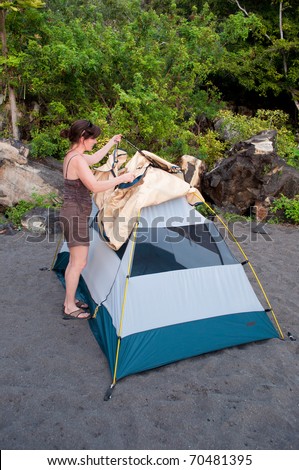 Woman demonstrates how to pitch a 2 person tent with a rain fly on a black sand beach campsite.