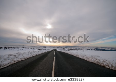 A cold winter road leading into the moorland wilderness of Yorkshire, England. There is deep snow which has been ploughed at the sides of the road
