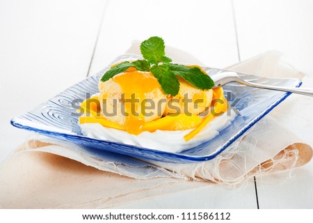 Mango ice cream with fresh mango and whipping cream in a blue glass plate