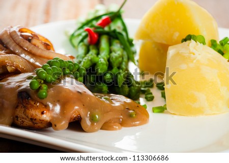 Freshly prepared piece of meat with onions and pepper sauce, cooked potatoes green asparagus and green pepper as a decoration on a white plate.