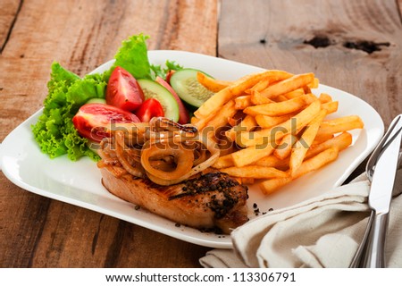 A menu with meat french potatoes roasted onion and salad on white plate