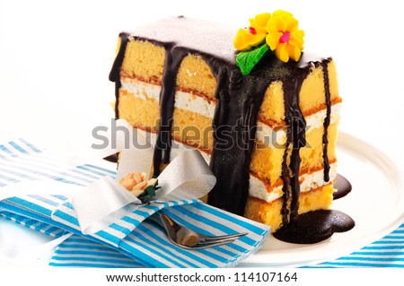 Small piece of three layer vanilla cake with cream and chocolate. Flower as decoration on the top. White background