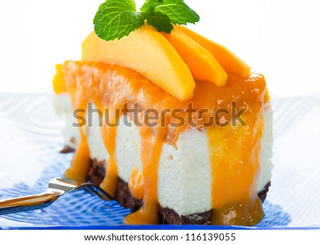 A piece of cheese cake with fresh mango and mango sauce on white background