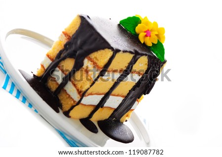 Small piece of three layer vanilla cake with cream and chocolate. Flower as decoration on the top. White background