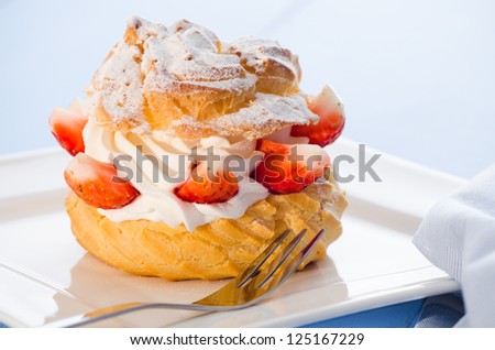 fresh cream puff with whipped cream and strawberries on white plate and light blue wood table