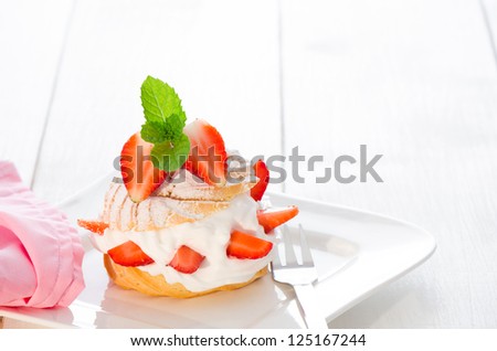fresh cream puff with whipped cream mint and strawberries on white plate and white wood table