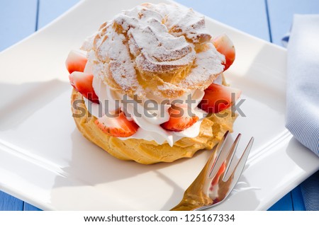 fresh cream puff with whipped cream and strawberries on white plate and light blue wood table