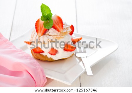 fresh cream puff with whipped cream mint and strawberries on white plate and white wood table