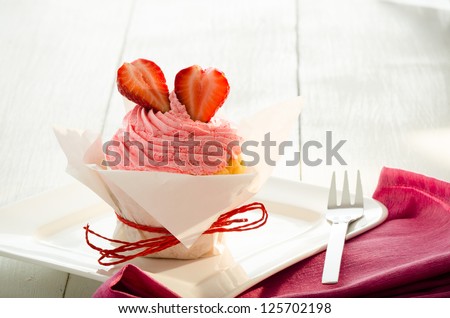 strawberry cupcake with white backing paper, red ribbon and two fresh strawberry on the top