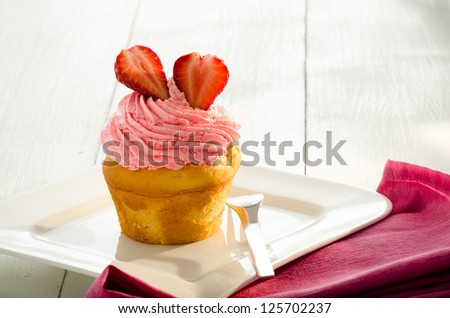 strawberry cupcake and two fresh strawberry on the top. White plate and fork