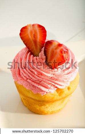 strawberry cupcake and two fresh strawberry on the top. White plate and fork