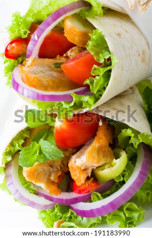 Chicken tortilla with fresh healthy salad ingredients including lettuce, onion, tomato and herb, close up view of two on top of each others
