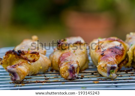 Three grilled chicken legs on a barbecue grill, outdoor in garden