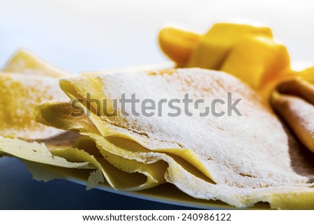 Freshly baked golden pancakes  or crepes neatly folded in a plate and served with fresh diced tropical fruit, close up view