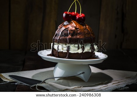 Delicious Chocolate Cake, Served on White Porcelain Tray, with Red Cherries on Top. Place on Top of Napkin at the Wooden Table with Spoon.