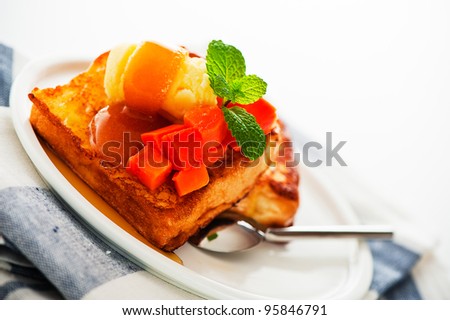 Two slices of french toast with papaya, vanilla ice cream, caramel sauce and mint leaf on a white background as a studio shoot