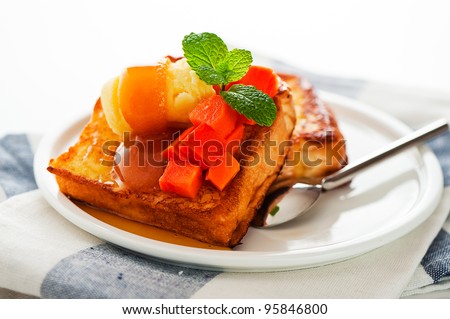Two slices of french toast with papaya, vanilla ice cream, caramel sauce and mint leaf on a white background as a studio shoot