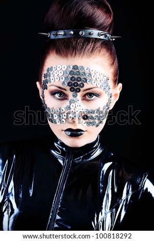 Conceptual shot of a woman in black glossy overall and metal buttons on her face.