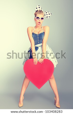 Beautiful young woman with pin-up make-up and hairstyle posing in studio with red hearts.