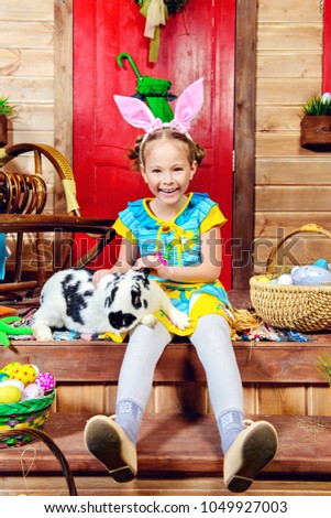 Happy little girl with bunny sitting on the porch of a wooden house. Easter holiday. Rural style, easter decoration.
